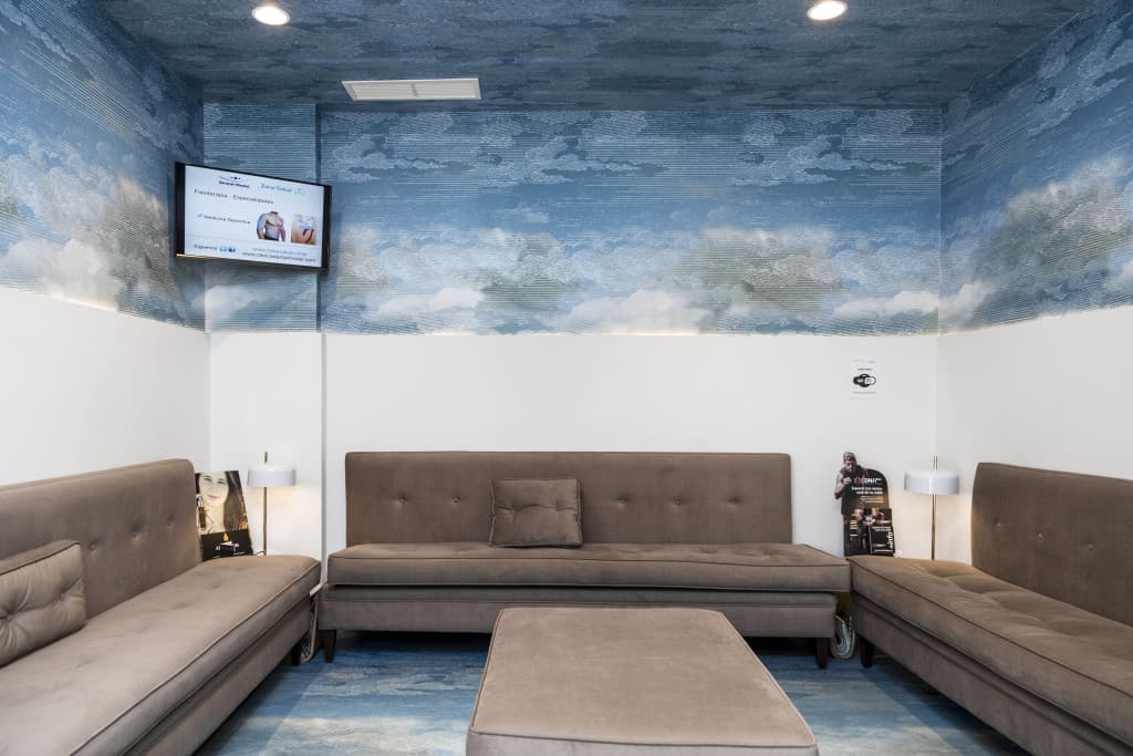 Sala de espera tranquila con techos de cielo despejado y sofás confortables en Dental Model
